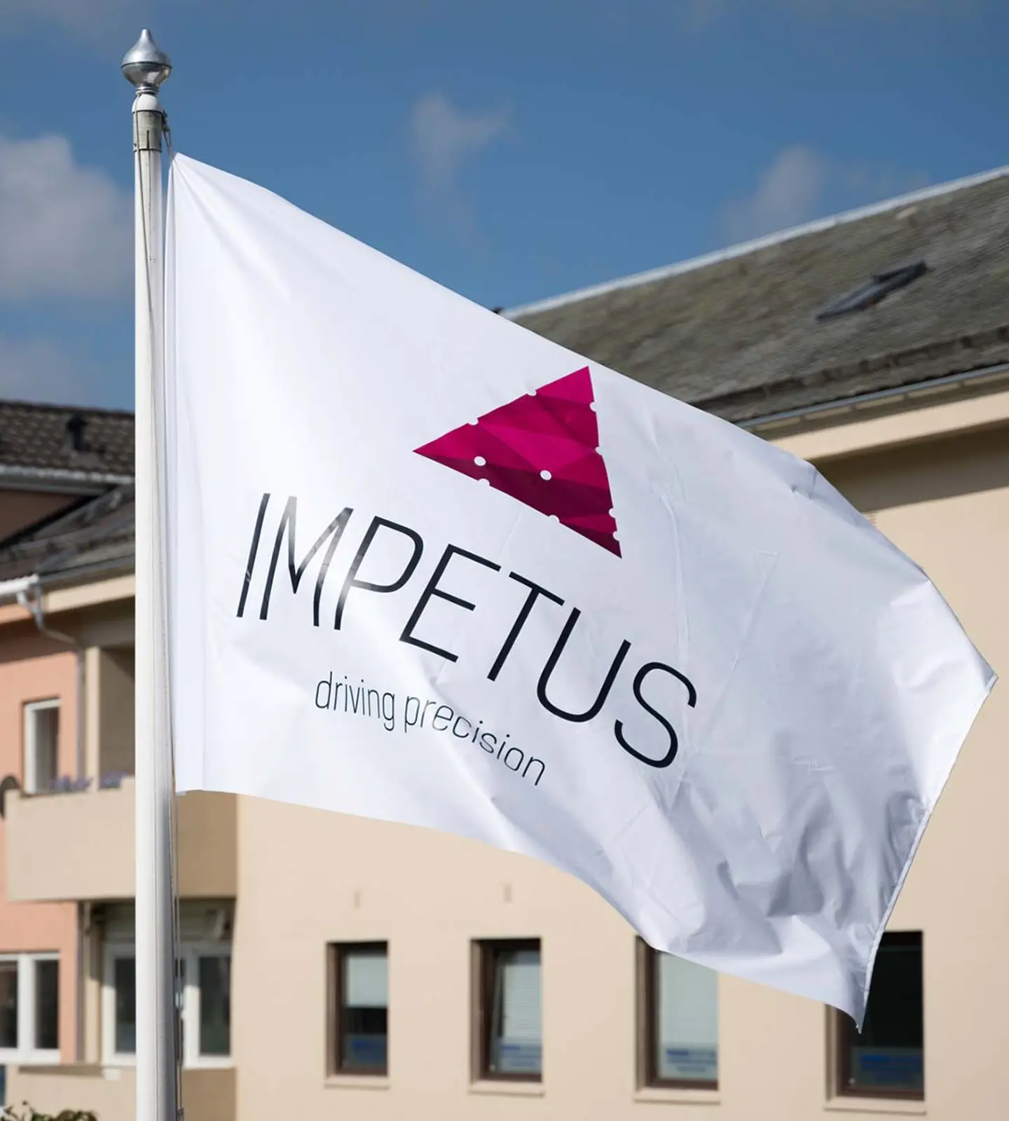 Hvitt IMPETUS-flagg med logoen «driving precision» vaier foran kontorbygningen i Flekkefjord