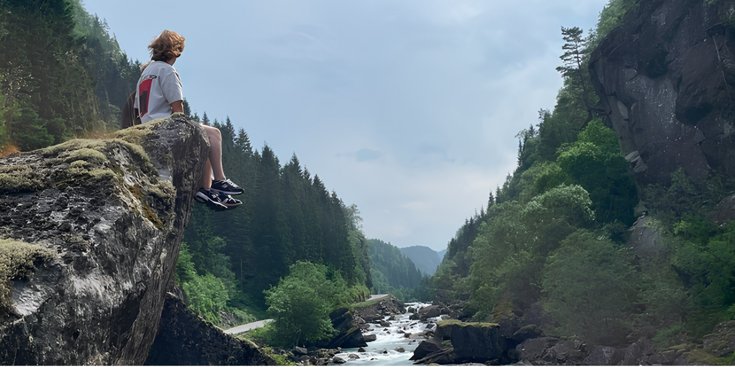 Sitting on the edge of a cliff looking out over a narrow gorge with a rushing river in Fossdalen