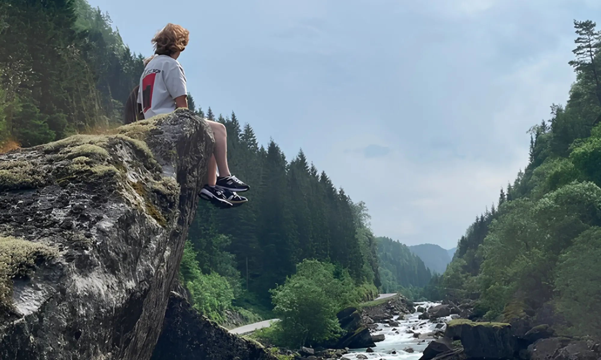 Sitting on the edge of a cliff looking out over a narrow gorge with a rushing river in Fossdalen