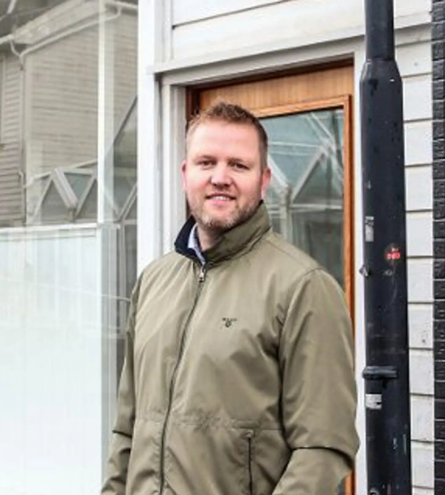 Eiendomsmegler fra Exbo står utenfor kontoret i Brogaten i Flekkefjord, ved siden av et "Til salgs"-skilt