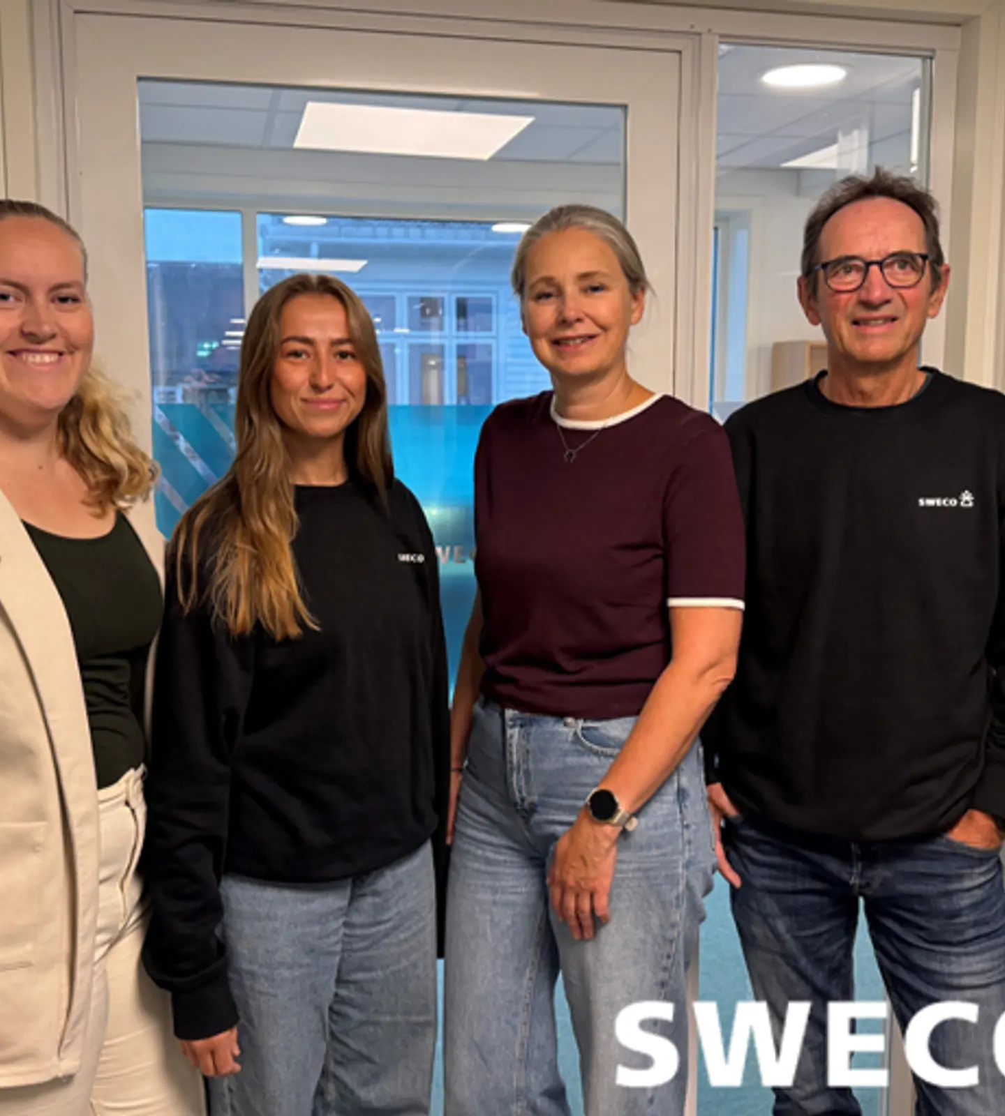 Fire ansatte i Sweco smiler foran et kontorlokale med Sweco-logo