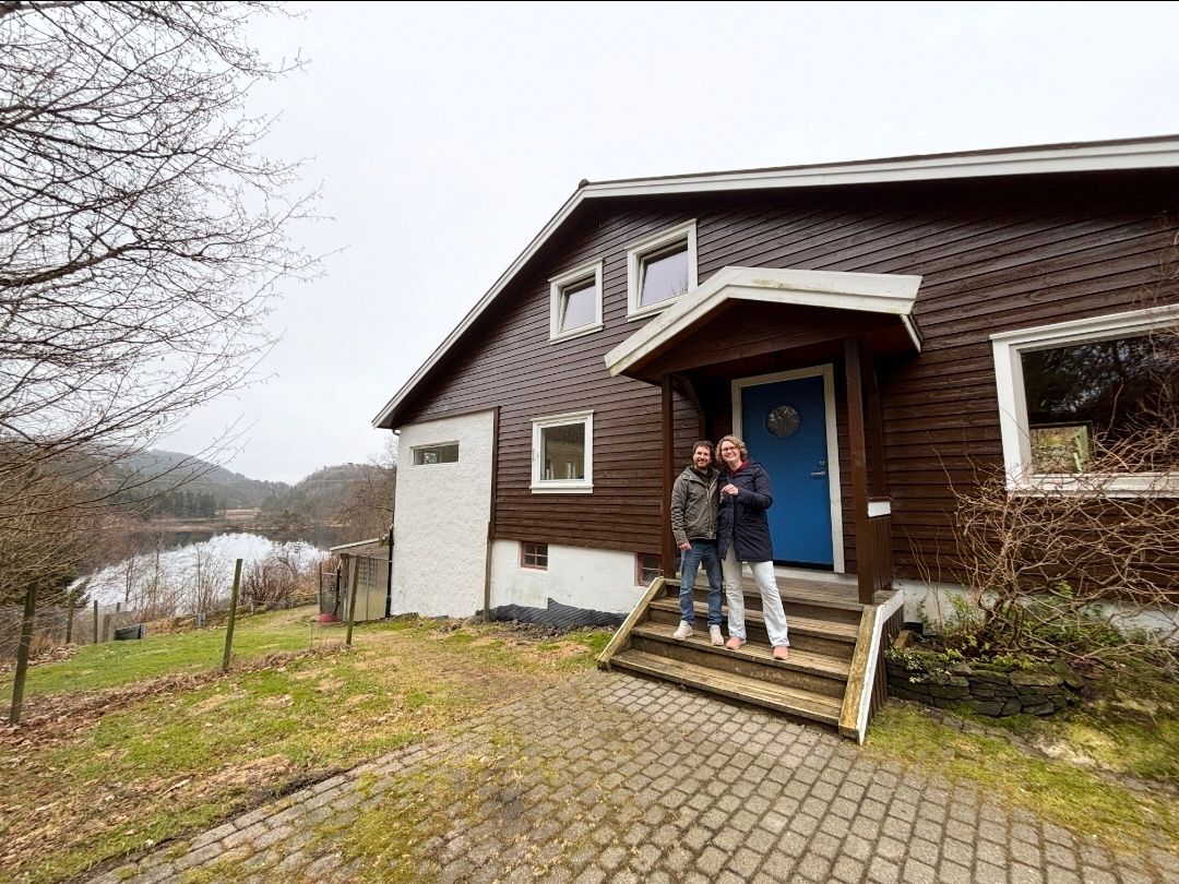 Jerry og Linda står på trappen foran huset sitt ved vannet i Feda.