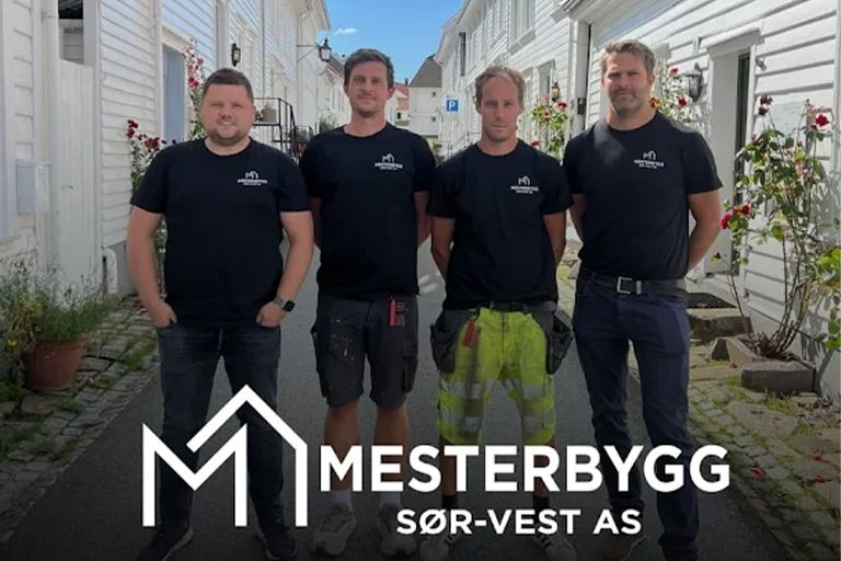 Four employees of Mesterbygg Sør-Vest AS standing together on a street with white wooden houses, in front of the company's logo