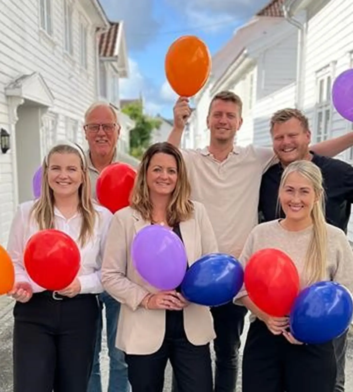Seks ansatte i Sparebanken Norge står utenfor hvitmalte trehus med fargerike ballonger