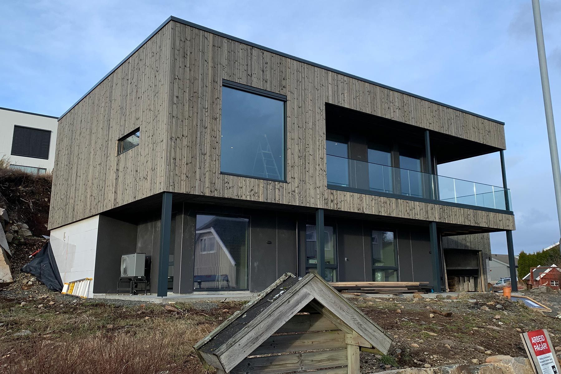 Enebolig med trekledning under oppføring, med stor terrasse og glassrekkverk i annen etasje