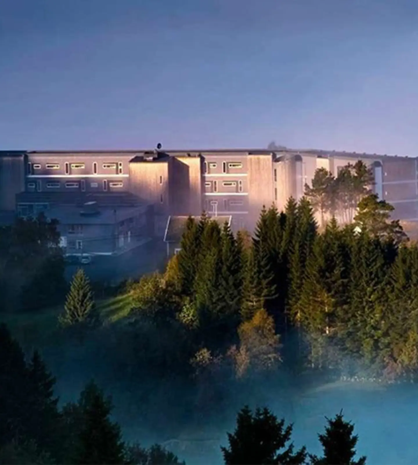Utsikten Hotell sett utenfra i kveldslys, med skogen og tåke rundt bygningen