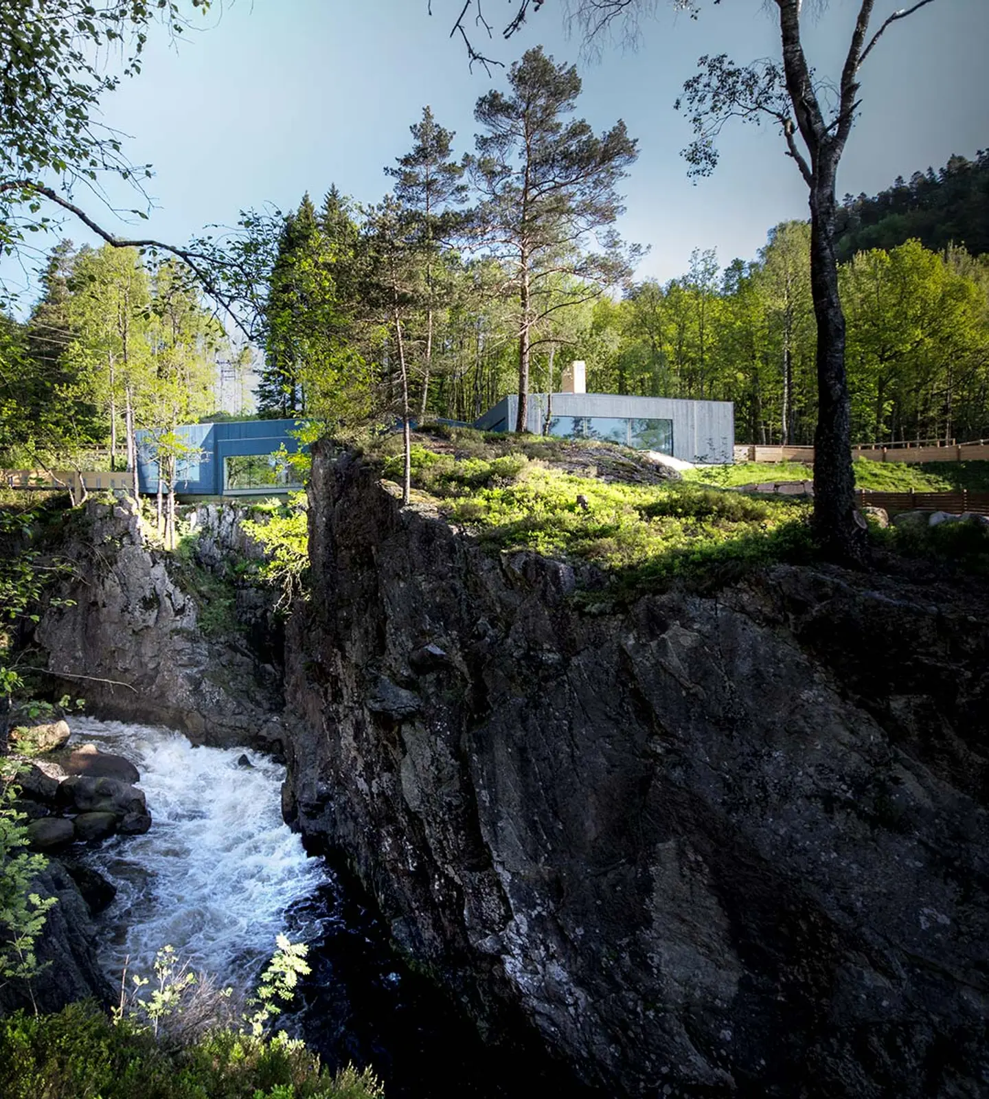 The wild salmon centre's building balances on the edge of the gorge above Kvåsfossen, surrounded by forest.