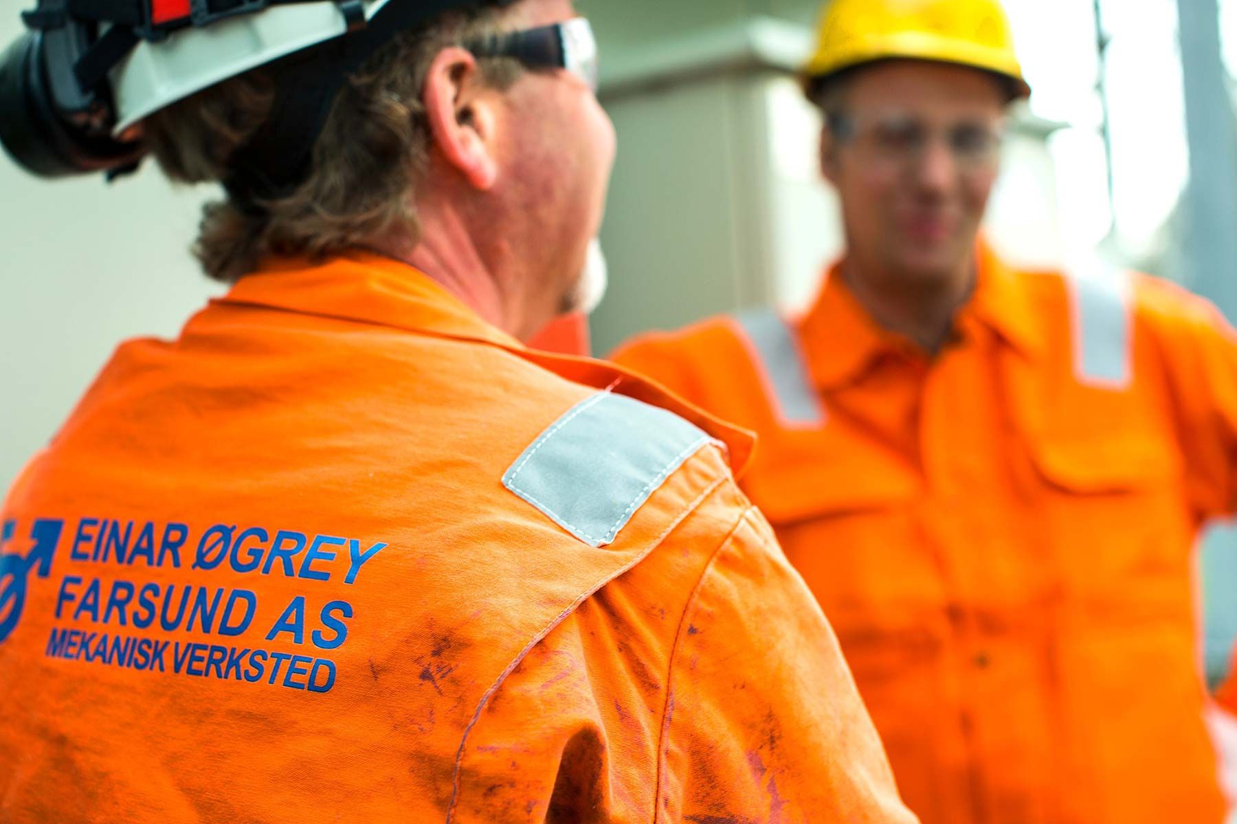 To ansatte i oransje arbeidstøy med Einar Øgrey Farsund-logo på ryggen, på et anlegg