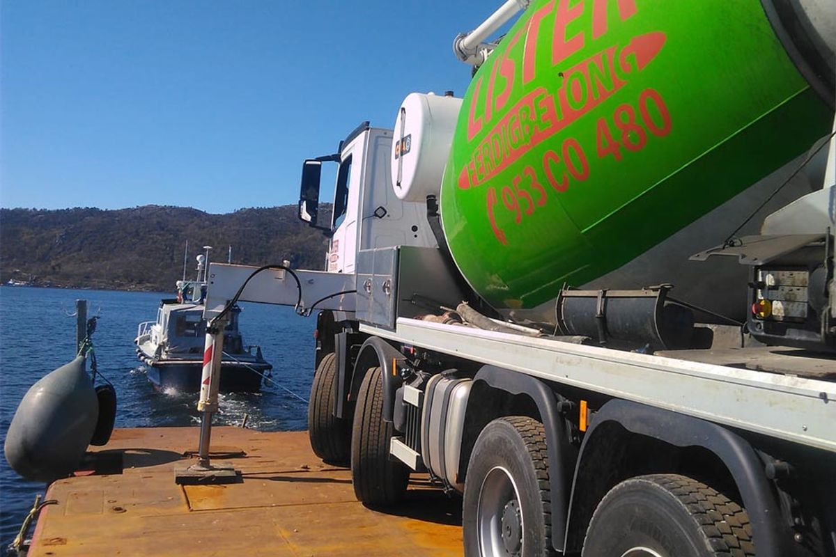 Betongbil fra Lister Ferdigbetong lastes fra kai, med fjorden og en mindre båt i bakgrunnen
